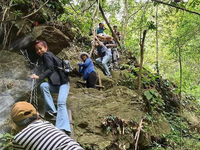 Group of hikers holding onto ropes on a steep, rocky forest trail.