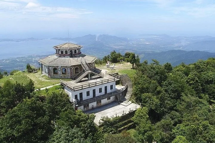 Luftaufnahme eines Aussichtsgebäudes auf einem üppig bewachsenen Berg mit Blick auf die Küste.