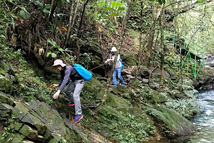 Hikers navigating a rocky edge next to a river using a rope.
