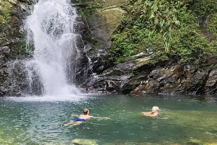 Zwei Personen schwimmen in einem natürlichen Becken am Fuß eines Wasserfalls.